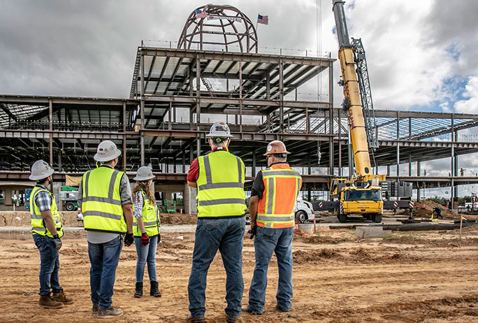 a group of four lean construction managers looking up at a large steel structure and crane