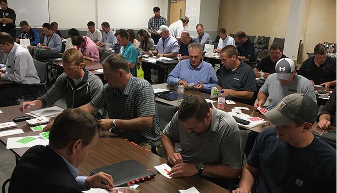 Dozens of people sit at desks in a classroom while taking part in an exercise using sticker dots.